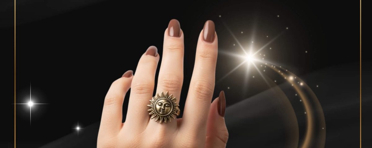 A hand with polished nails, sun-themed ring, and chain bracelet on a decorative background.
