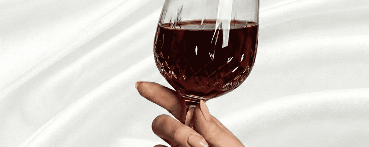 Hand with luxury nails holding a wine glass on a silk background.